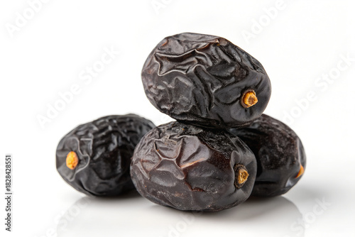 A photo of dark, wrinkled dates piled in a small, cream-colored bowl on a white surface, softly lit, creating a simple, inviting still life.