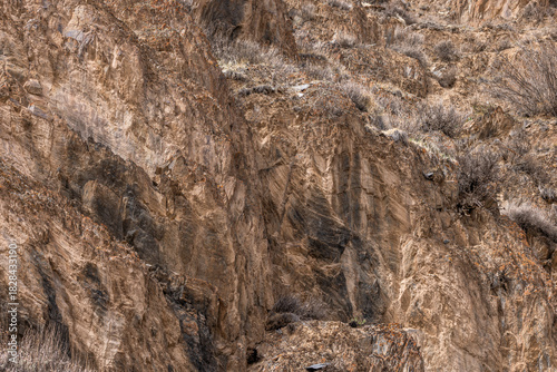 Rugged rock formation stands prominently in a desolate mountainous region. The natural environment captures the austere beauty of the landscape under bright daytime light.