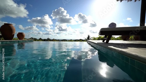 Serene pool view with blue water reflecting the sky, deck with lounge chair, and blooming red flowers