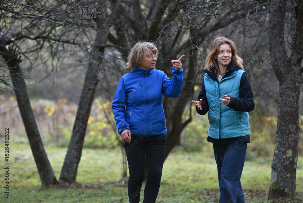 Fototapeta premium Mother and young adult daughter talking and gesturing while walking outdoors in autumn