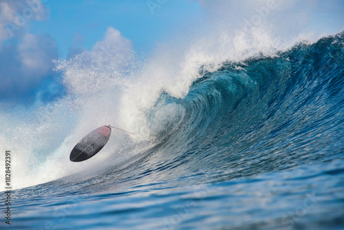 Surfboard thrown by towering blue wave, board flipping midair with frothy spray and curling barrel at dawn light