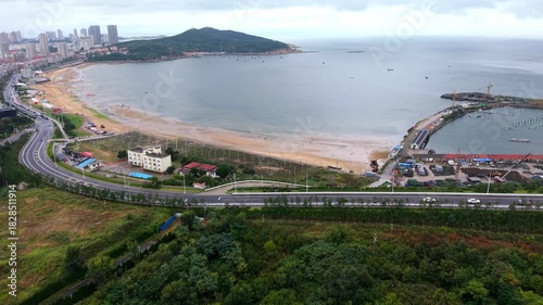 Curved golden sandy bay and fishing harbor with green hills, aerial China