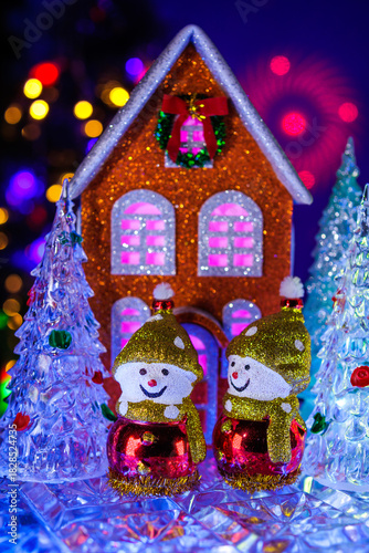A close-up of glass Christmas trees around an orange house with two snowmen in front