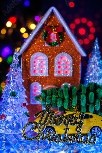  A close-up of glass Christmas trees around an orange house with a yellow car with a Christmas tree on the roof and letters in front