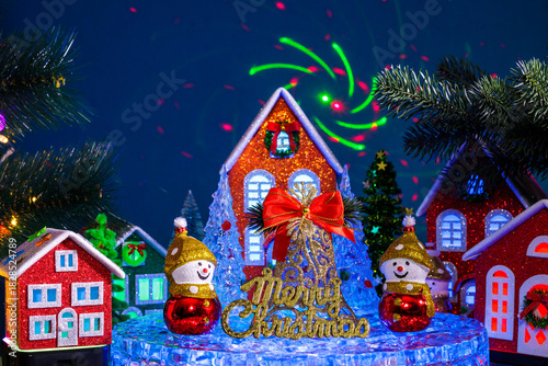 In the center of the Christmas village there is a golden bell with letters and snowmen with glass Christmas trees