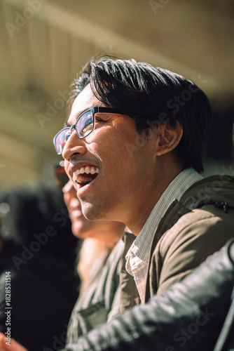 Shocked male fan wearing eyeglasses with mouth open watching game from stadium stand