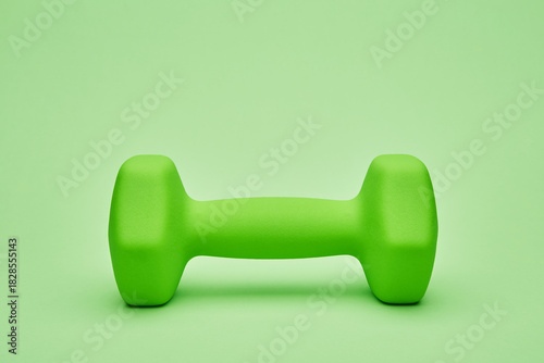 Bright green dumbbell placed on plain background for exercise and fitness concept