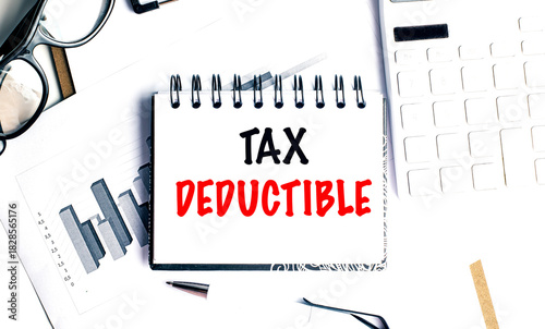 Tax deductible phrase on spiral notebook with financial documents, calculator, pen and glasses