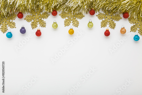 Beautiful shiny golden tinsel, snowflakes and colorful baubles on light gray table background. Closeup. Christmas decoration. Empty place for text. Top down view.