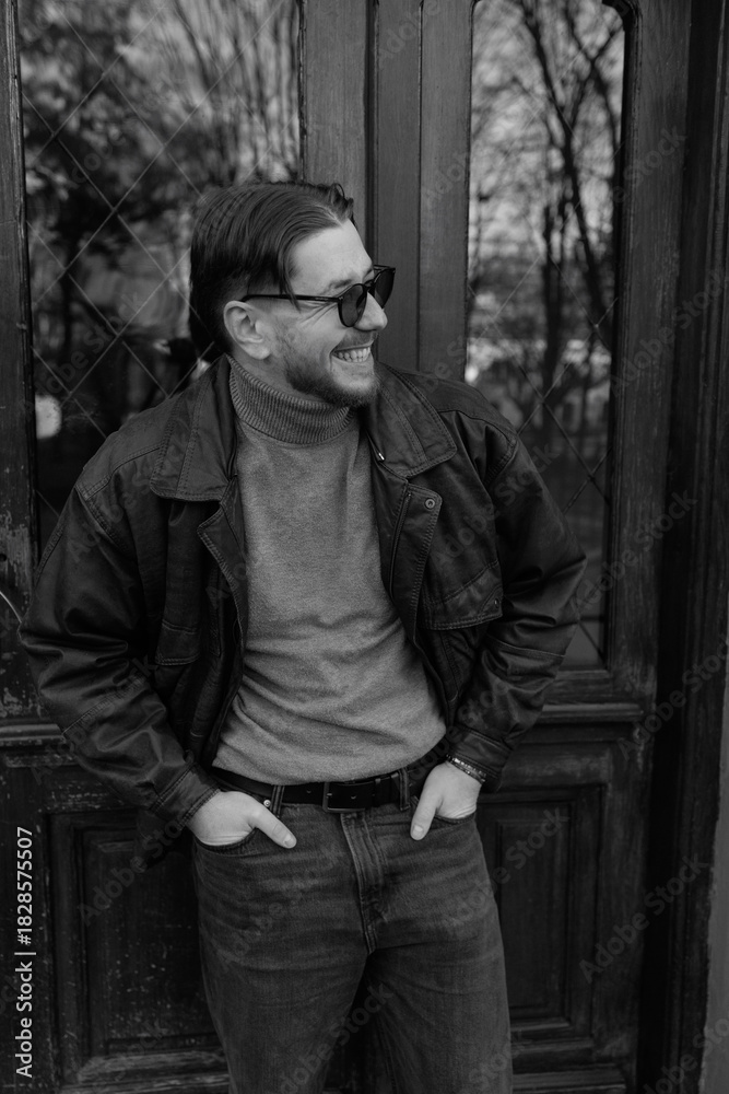 Obraz premium Stylish young man wearing glasses posing in front of a modern building, black and white portrait photograph