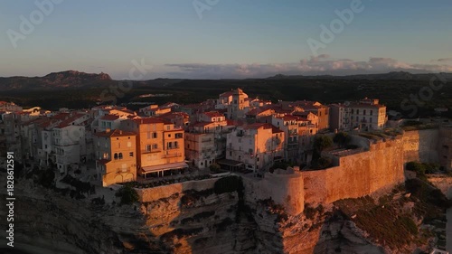 Expansive Aerial Drone Approach Shot Gliding Over the Mediterranean Sea Towards the Historic Bonifacio Citadel City Perched on Dramatic White Limestone Cliffs at Golden Hour Sunrise, Corsica, France.