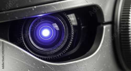 Close-up of a glowing blue lens resembling a robotic eye, surrounded by intricate mechanical gears and a textured, scratched metallic casing, evoking futuristic technology.