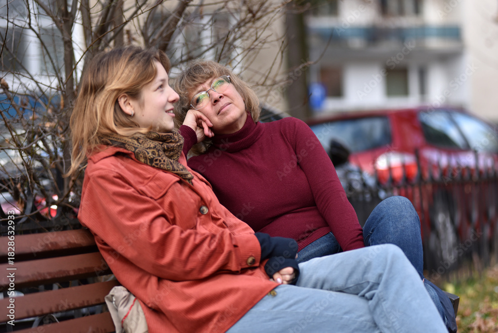 Fototapeta premium Teenager daughter and mother resting on a park bench in autumn