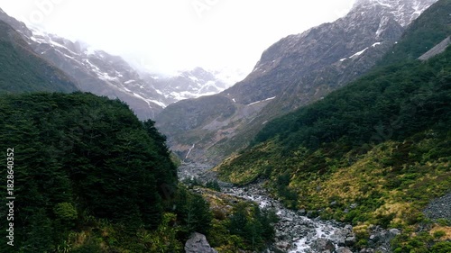 Aerial view of a river cascading through rocky terrain into lush green valleys under a cloudy sky.