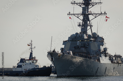 
GUIDED MISSILE DESTROYER - US Navy ship maneuvers in the port assisted by a tugboat 