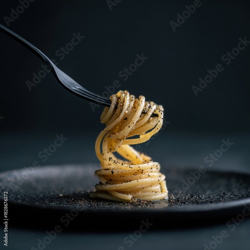 A fork holds twirled pasta on a plate, sprinkled with a dark savory powder.