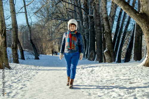 Confident older woman enjoying brisk walk through snowy woodland alley on bright day