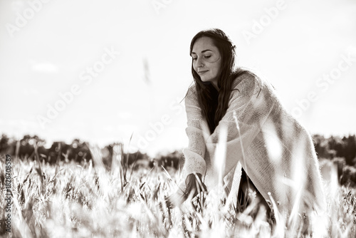 Young woman gently touching rye field in soft natural light with serene expression