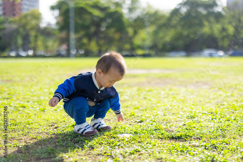 Baby squatting carefully while looking at green grass