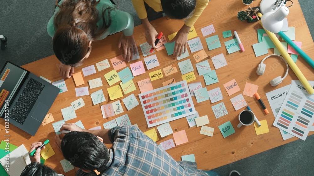 Obraz premium Time lapse of business team with casual outfit looking laptop screen and sharing idea. Aerial view of manager working and checking color palette at table with sticky notes and headphone. Symposium.