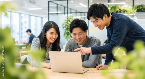 Smiling Asian business team working together on laptop in modern office. Collaboration and teamwork.