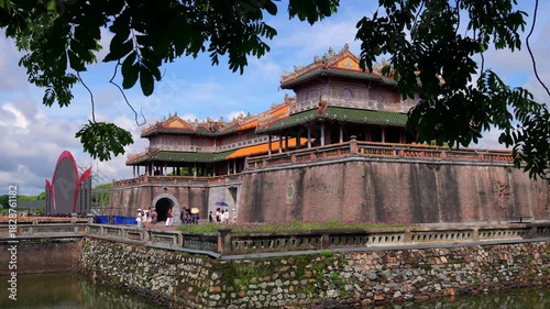 The iconic Noon Gate rises majestically over a green moat, framed by vibrant yellow sunflowers and frangipani branches.