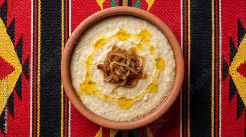 Top view of traditional Saudi Jareesh dish with caramelized onions and ghee in clay bowl on red Sadu background
