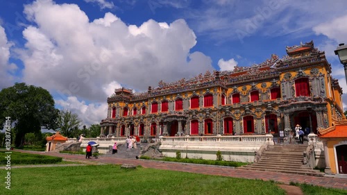 Majestic Kien Trung Palace featuring vibrant yellow walls, ornate ceramic mosaics, and striking red shutters against a cloudy blue sky.