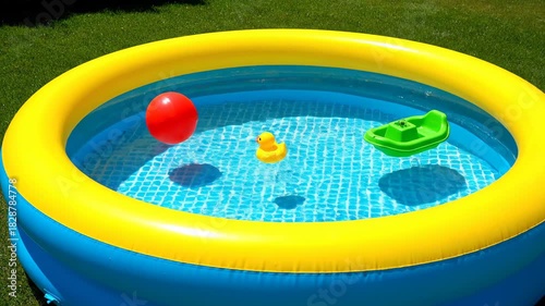Bright inflatable kiddie pool with yellow trim filled with clear water and playful toys including a rubber duck and a small boat on a sunny day