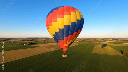 Colorful hot air balloon drifting peacefully above green fields under a clear blue sky