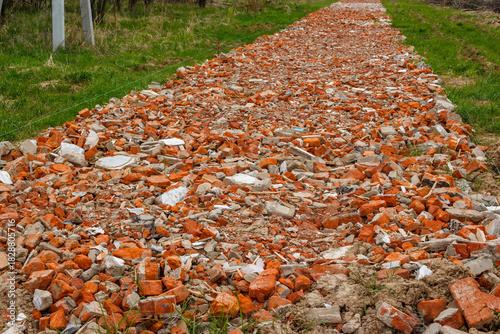 Crushed red brick rubble creating a makeshift roadbed or base for a future pathway in a grassy field during springtime construction