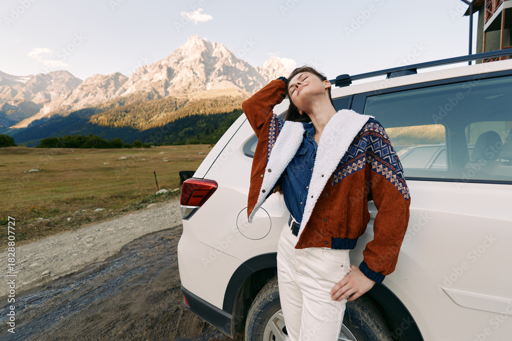 Fototapeta premium Woman by car on mountain road wearing warm jacket, looking up at peaks, travel and adventure scene in nature with SUV and scenic landscape for outdoor lifestyle portrait.