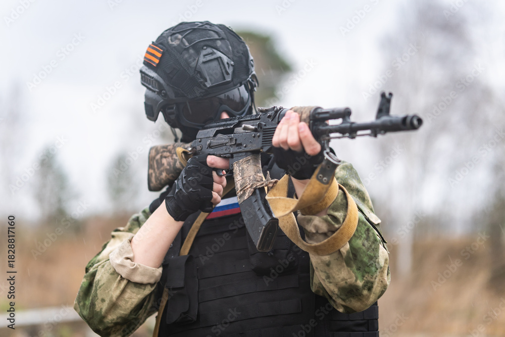 Obraz premium Russian special forces soldier holds a Kalashnikov assault rifle in his hands and stands in sight. Russian assault military forces soldiers at combat action. military exercises in the Russia army.