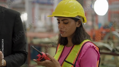 Indian woman engineer waiting for radio response, holding walkie-talkie. Caucasian man manager checking digital tablet. Factory team discussing communication delay or connection issue.