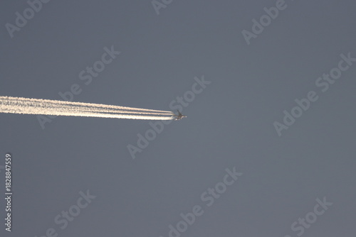 A plane flies in the sky before sunset with its exhaust out.