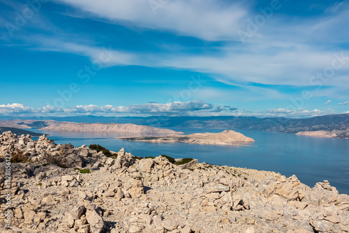 Fototapeta Naklejka Na Ścianę i Meble -  A scenic view of rocky stone piles on the barren slopes of Kamenjak mountain overlooking the deep blue Adriatic Sea and the Velebit mountain range on the mainland from Rab island in sunny Croatia.