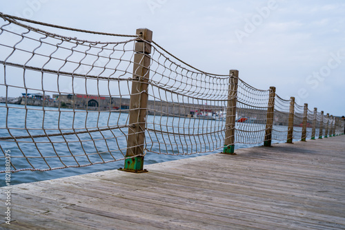 Wooden Boardwalk with Rope Net Fence by the Water on a Cloudy Day