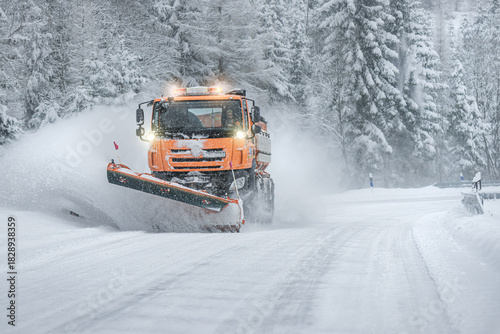 Snow plow clear and sprinkles snowy road in a snowstorm.