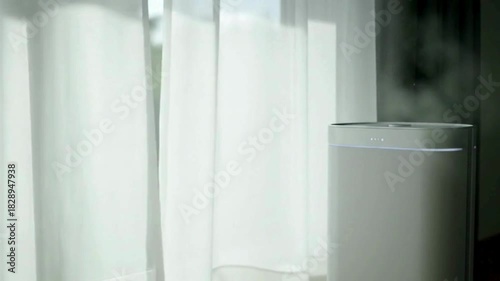 Modern humidifier gently misting beside sheer curtains in a bright room