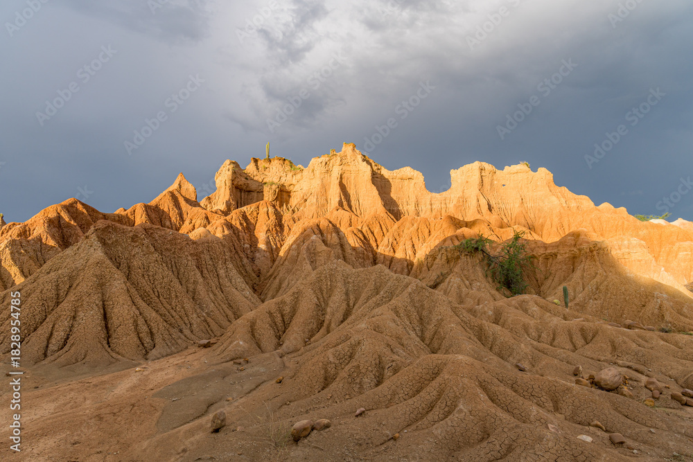 Naklejka premium Sunlit peaks of Tatacoa Desert mounds under brooding gray clouds