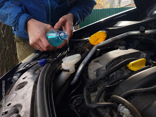 Pouring coolant into car engine for maintenance on a sunny day
