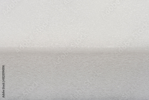 A horizontal close-up shot showing the edge of a bright white, fine-pored plastic foam or sponge material