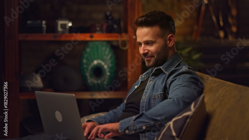 Businessman working from home on laptop computer. Happy young man sitting on couch in home office with laptop.