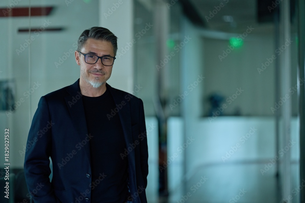 Obraz premium Business portrait - businessman standing on office corridor. Happy middle aged, mid adult, mature age man smiling. Entrepreneur in modern workplace. Copy space.