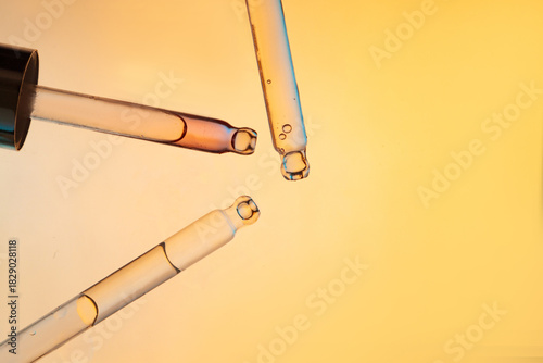 Three glass pipettes with facial serum on light orange background. Frontal close-up view of liquid gel or essential oil, banner for advertising anti-aging cosmetic product
