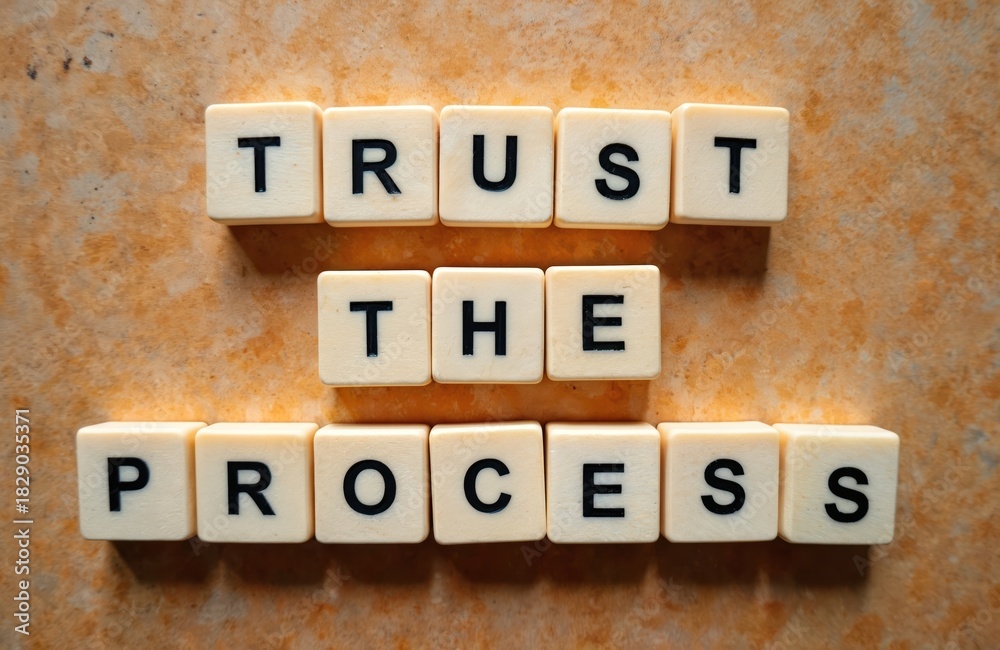 Naklejka premium Scrabble tiles spell out TRUST THE PROCESS on textured orange background. Motivational phrase for business, personal growth, patience, and perseverance.