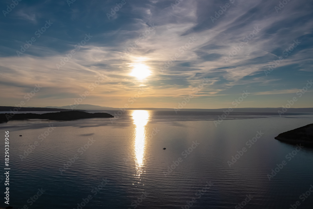 Fototapeta premium A breathtaking sunset illuminates the calm Adriatic Sea near Lopar on Rab Island, Croatia, casting a golden reflection on the water with silhouetted islands and mountains in the scenic distance.