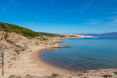 Fototapeta Naklejka Na Ścianę i Meble -  A secluded sandy beach surrounded by unique sandstone cliffs lies near Lopar on Rab Island, Croatia, inviting tourists to relax by the calm blue Adriatic Sea under a bright and sunny summer sky.