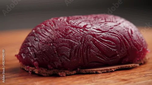 A glossy, maroon-colored dome sits atop a dark cracker, on a light wood surface, under muted lighting