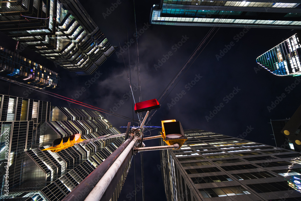 Fototapeta premium A lone traffic signal rises into a canyon of towering glass, its red glow contrasting with the cold geometry of the surrounding skyscrapers.